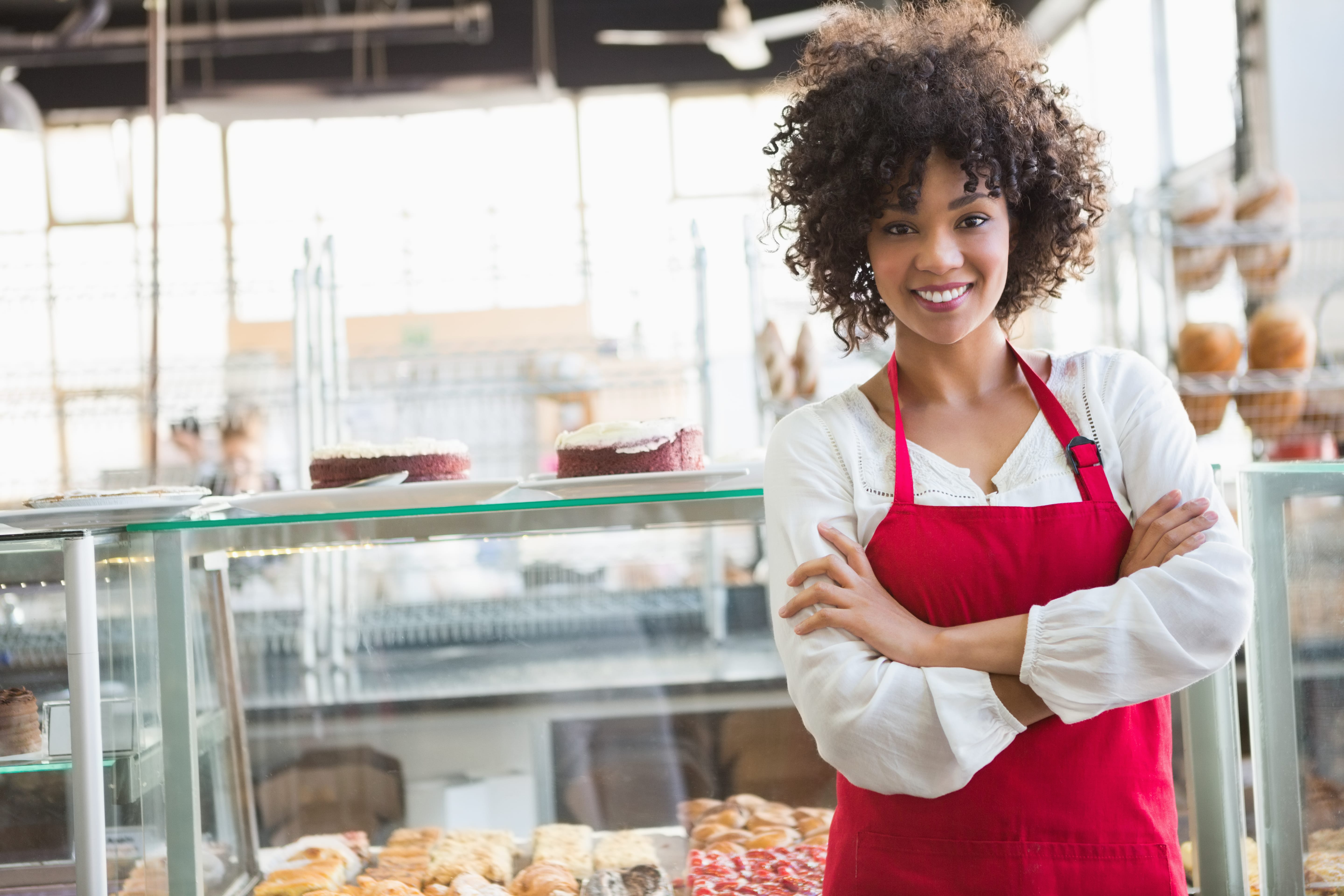 Employee in an apron smiling in front of a pastry display case.
